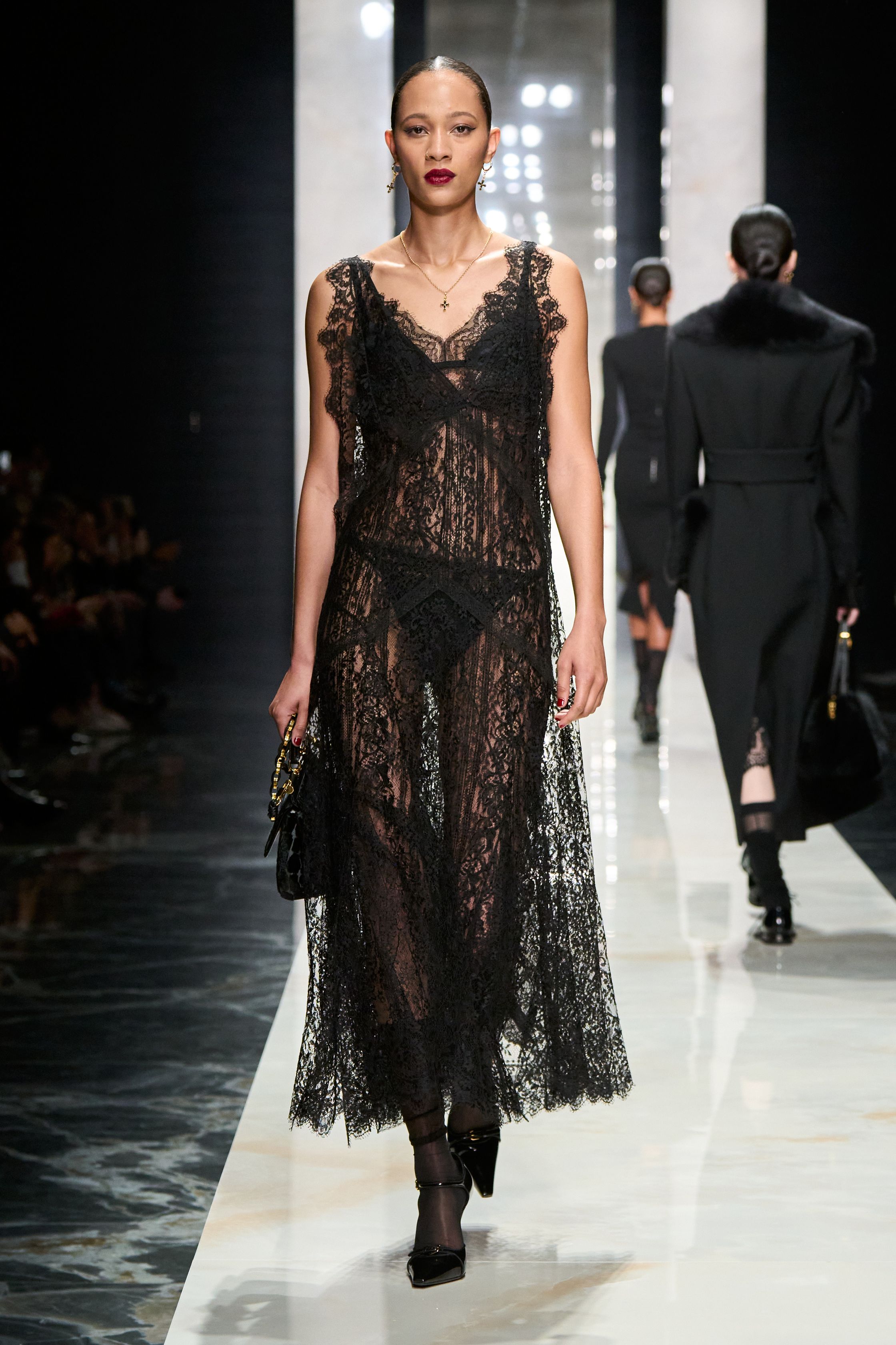 Dolce & Gabbana在本季回归品牌标志性的性感意大利美学，通过黑色蕾丝、修身西装与透视礼服塑造极具戏剧张力的女性形象。系列以黑色为核心色调，结合紧身胸衣结构、透明蕾丝裙与宽肩西装，形成刚柔并济的视觉语言。皮草外套与复古帽饰则增添奢华氛围，使整体造型在性感与优雅之间保持平衡，呈现出典型的意大利电影般的华丽气质-顽石频道趋势研究